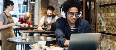 Man working on a computer wearing headphones in a cafe