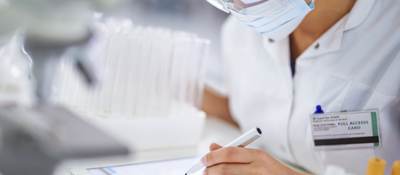 Female medical professional wearing protective eyewear and facemask making notes on electronic device