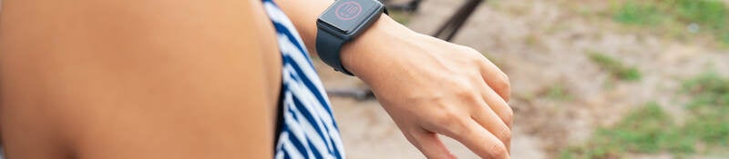 Young woman with wearable patch on arm checking a smartwatch to see her blood sugar level.