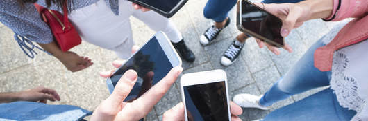 A group of young adults scrolling through their cell phones. 