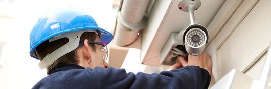 Man in hard hat on a ladder installing an outdoor security camera