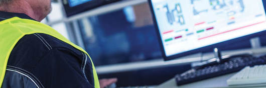 factory worker at a control panel pressing and looking at a monitor