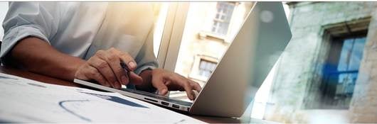 Hands typing on a laptop with windows in the background