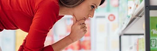 Brown-haired woman looks carefully at a shelf filled over-the-counter medications.