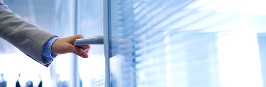 photo of a hand opening an office door, with people in background.