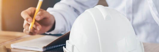 Photo of a person making notes, hard hat in foreground