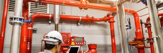 Engineer with tablet checks red generator pump for water sprinkler piping and fire alarm control system.