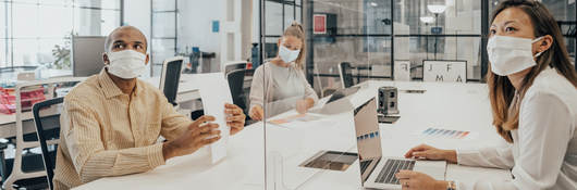 People in open office environment working separated by transparent dividers 