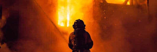 A firefighter sprays water on the outside of a burning building