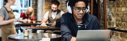 Man working on a computer wearing headphones in a cafe