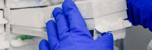 Gloved hands removing a white box from frost-covered medical freezer.