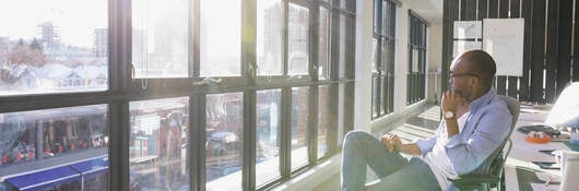 Pensive businessman looking out sunny office window