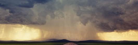 Road leading to a storm with clouds on the horizon.