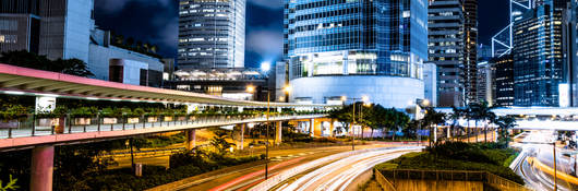 A multi-lane highway is brightly illuminated by roadway lighting, with a modern cityscape on the horizon.