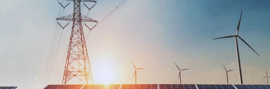 Large electric line tower over solar panels with sun in the background