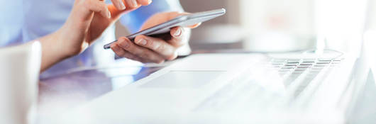 woman using a mobile phone in front of a laptop computer