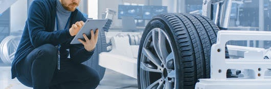 Engineer in an automotive laboratory works on a tablet and evaluates a car prototype