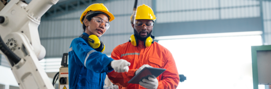 Engineers talking in a factory, with robotic arm in foreground