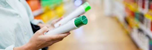 Person comparing green and white plastic bottles in a supermarket