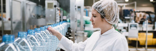 person inspecting conveyor belt of plastic water bottles