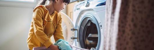 Little girl unloading the washing machine while helping her mom with laundry at home