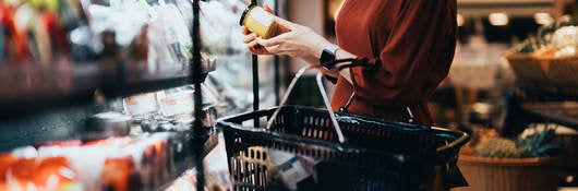 Cropped shot of young Asian woman carrying a shopping basket, standing along the dairy aisle, reading the nutrition label on the bottle of a fresh organic healthy yoghurt.