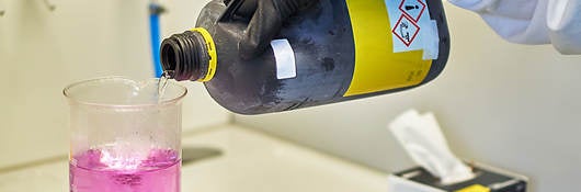 a lab tech pouring hazardous chemical into a beaker