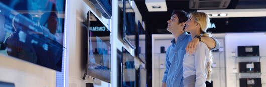 A couple in an electronics store looking a televisions