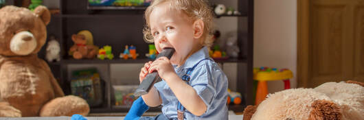 Toddler sitting while chewing on a tv remote