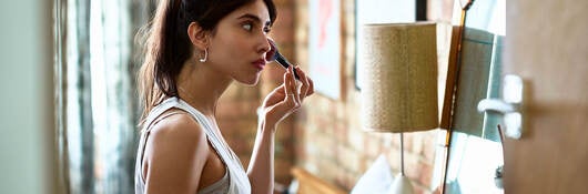 Person applying makeup with a brush and holding toast