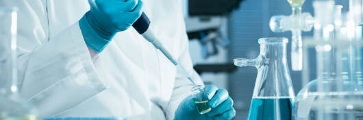 A laboratory technician using a pipette, testtubes, and flasks with blue liquid