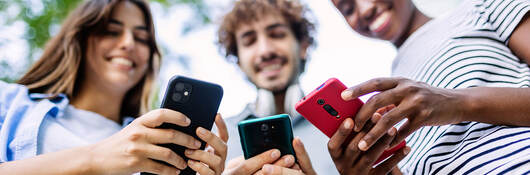 Three smiling friends outdoors and holding cellphones