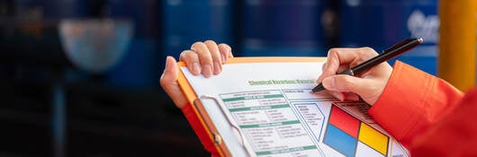 Worker checking chemical hazardous communication form on a clipboard.