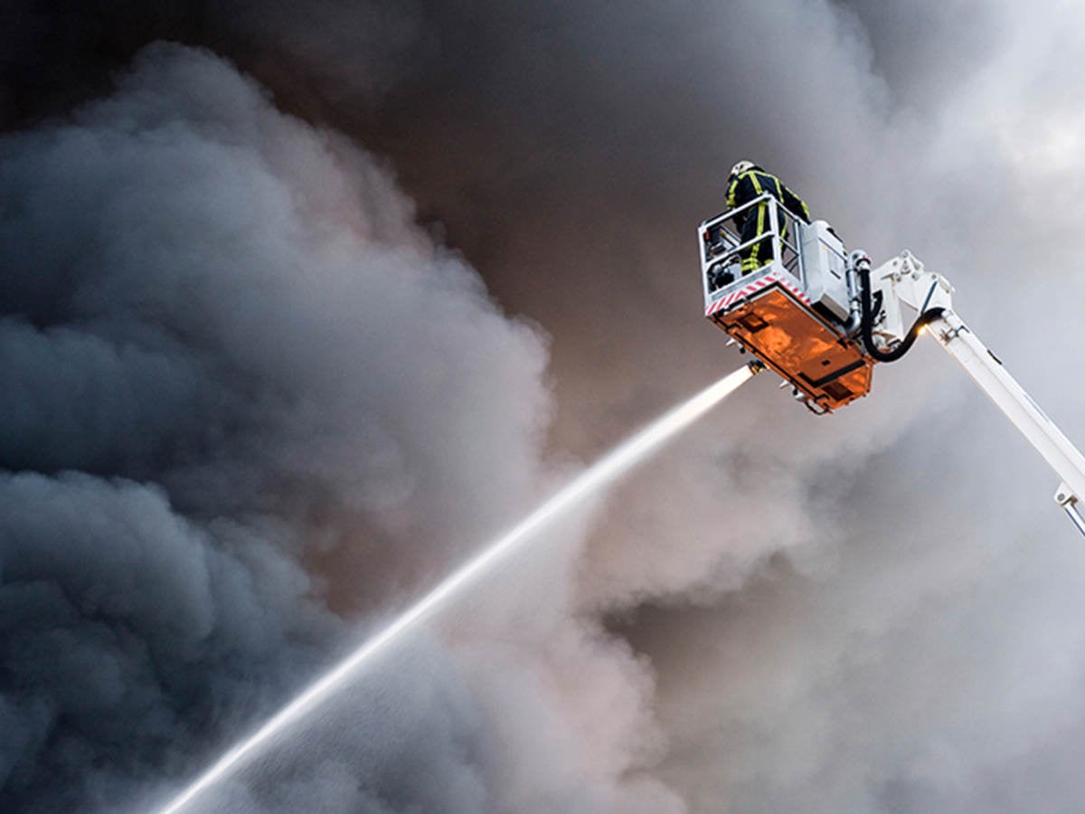 Firefighter on aerial ladder spraying hose against smoky sky