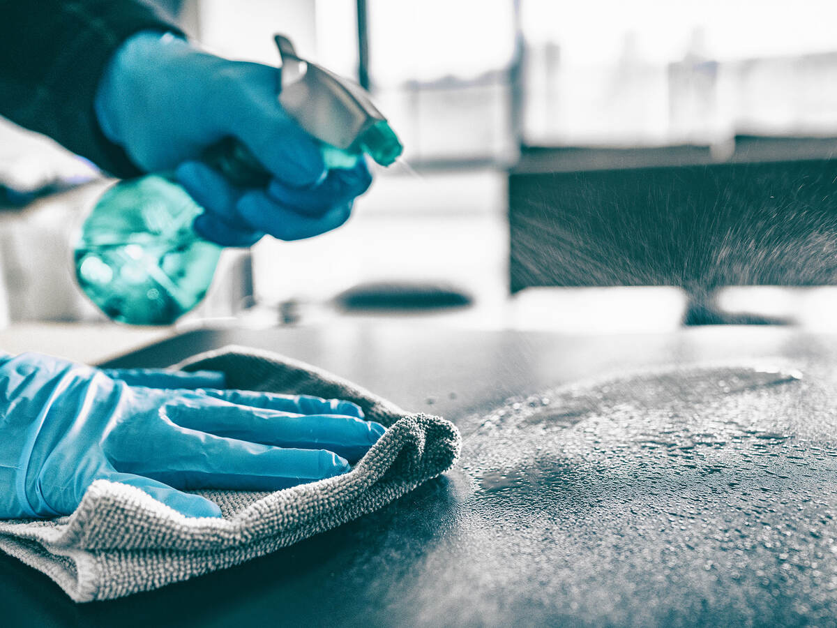 A person wearing gloves and cleaning a surface with spray cleaner