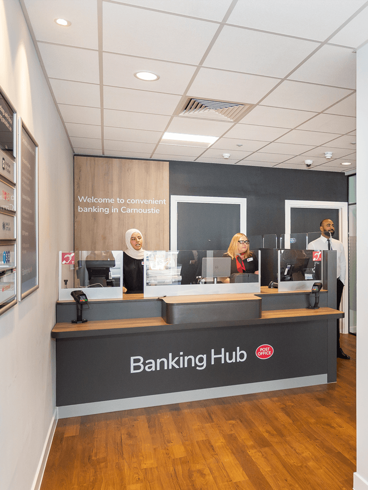 A Banking Hub counter staffed by 2 people, with card readers and desktop computers