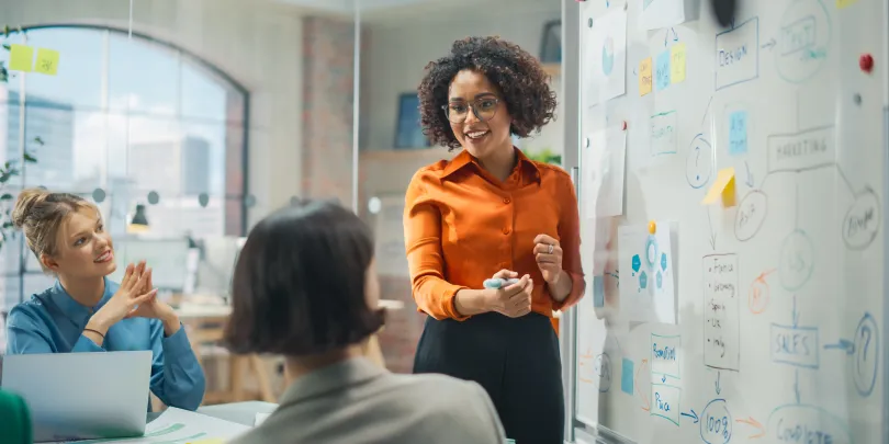 A woman in an orange blouse presenting at a marketing strategy session to advertisers.