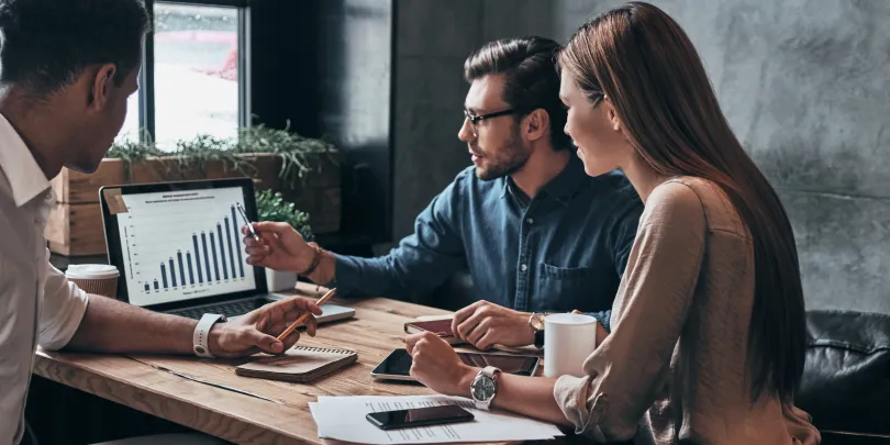 Three performance marketers looking at a laptop screen and analyzing real-time reporting and insights.