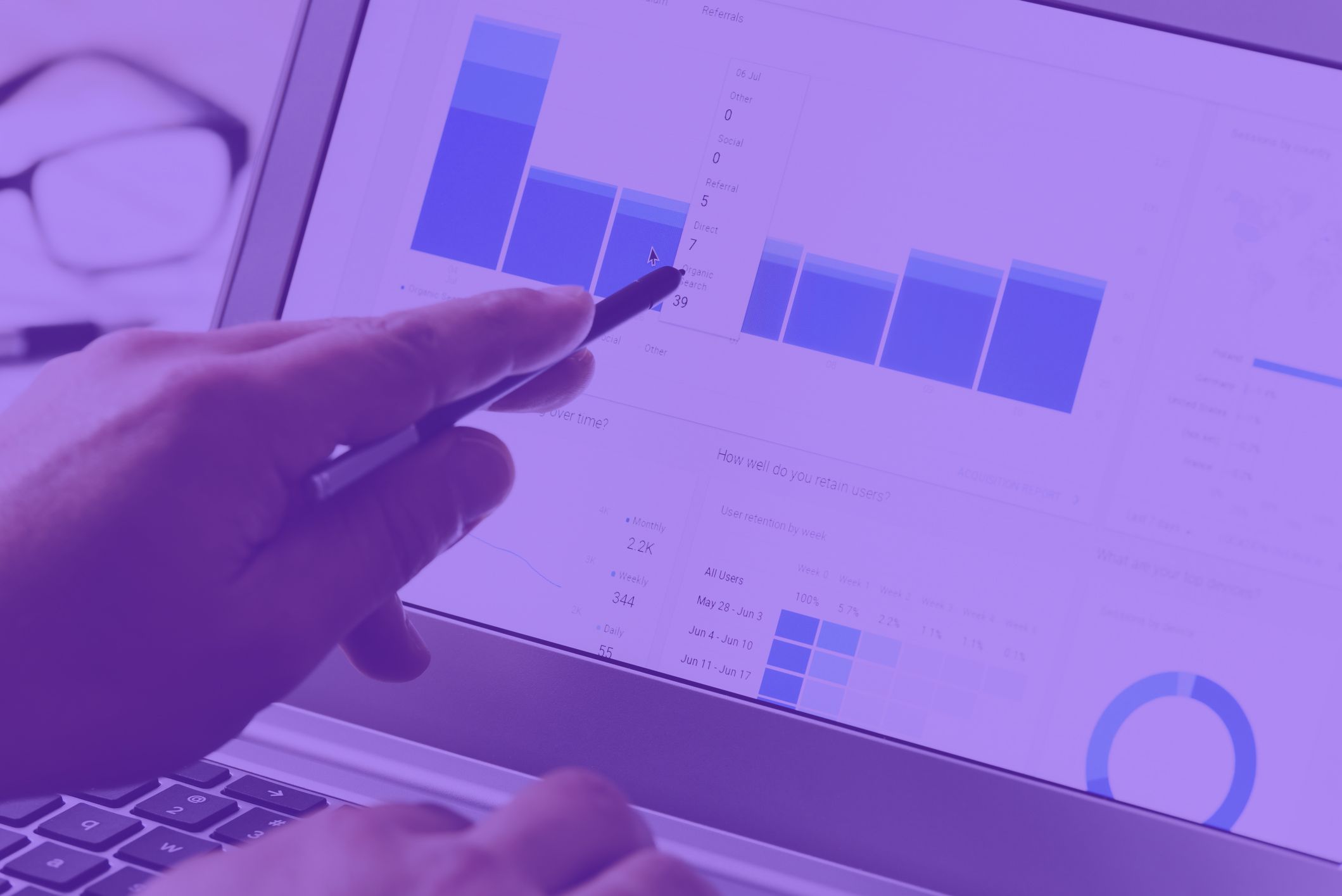 Someone pointing with a pen at a laptop screen displaying graphs and charts