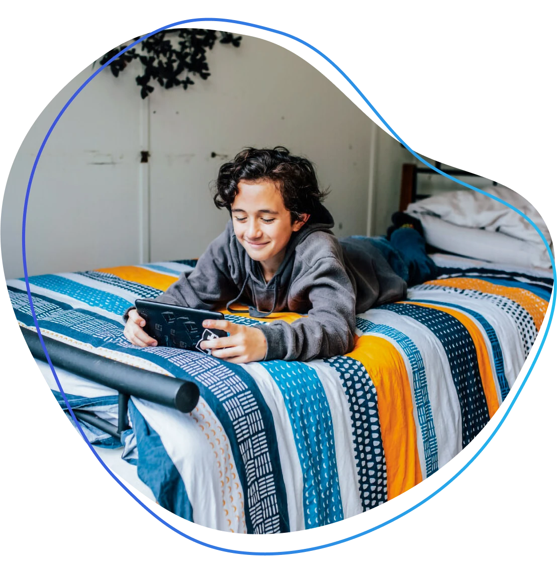 A young Māori boy, on his bed smiling and playing on a tablet device