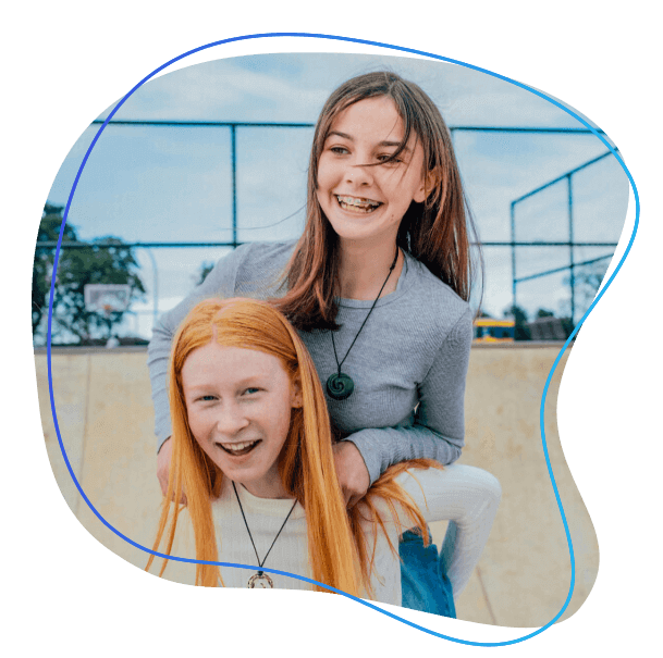 Two smiling young girls. One is giving the other a piggy back ride