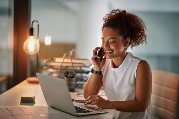 woman smiling at laptop holding phone