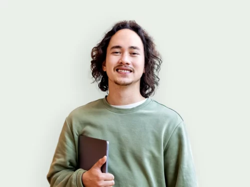 Young man in green sweatshirt holding his laptop under his arm