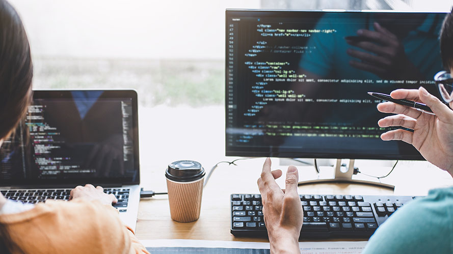 Unseen user working on a laptop with programming code displayed onscreen.