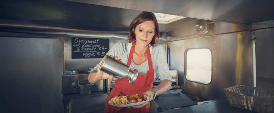 Junge Dame bereitet Currywurst Pommes zu, in einem Foodtruck