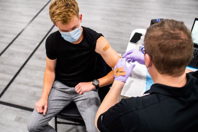 Photo: Mackenzie Fallon of Student Health Services gives a vaccine to Alexander Bade, a white man with blonde hair and a black shirt, during an immunization clinic.