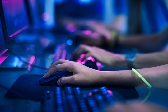 Close-up On Row of Gamer's Hands on a KeyBoard.jpgs, Actively Pushing Buttons, Playing MMO Games Online. Background is Lit with Neon Lights.