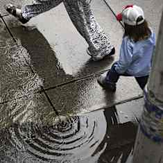 View from above of pedestrians stepping over puddles on a sidewalk.