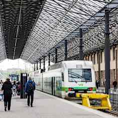 People walking on platforms near a parked green-and-white train under a roof at Helsinki's central railway station.