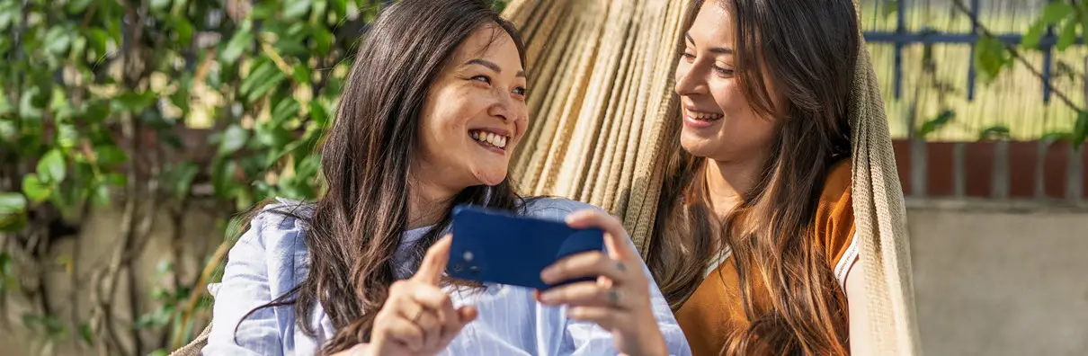 Deux amies souriantes devant leur smartphone, elles profitent du réseau mobile Bouygues Telecom